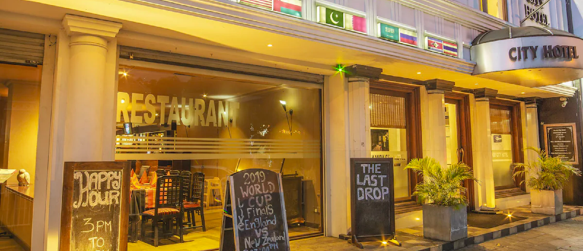 A brightly lit city hotel and restaurant entrance in Kandy, Sri Lanka, with happy hour signs.