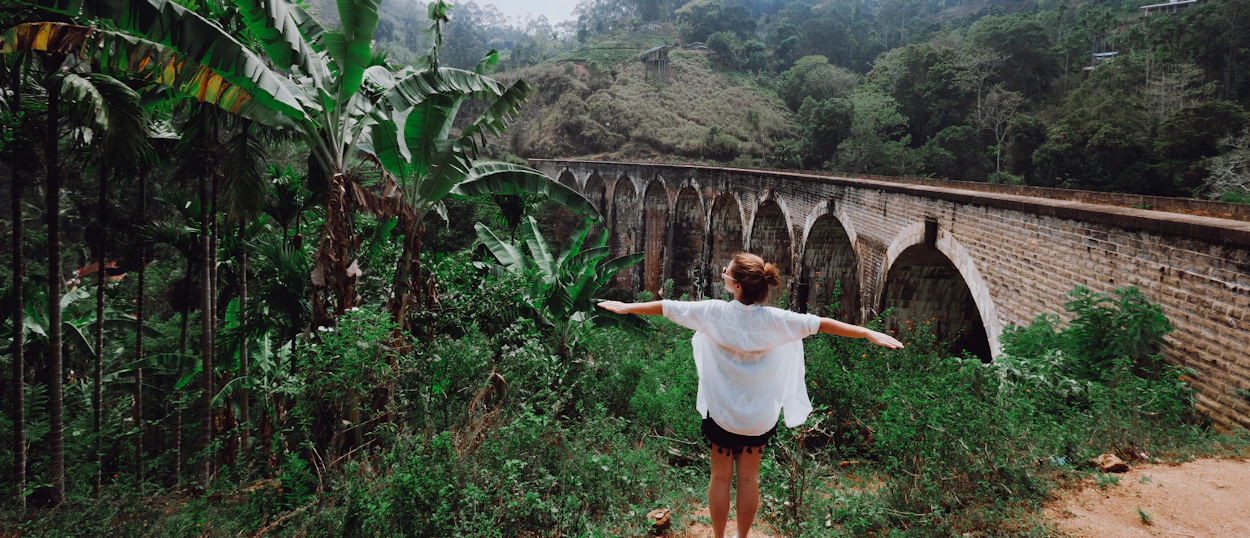 A person with outstretched arms stands before the iconic Nine Arch Bridge in Ella, Sri Lanka.