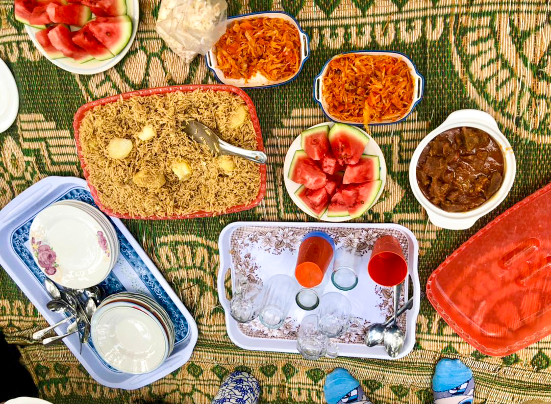 Vibrant communal lunch with rice, stew, and fresh watermelon served on a green mat in Zanzibar.