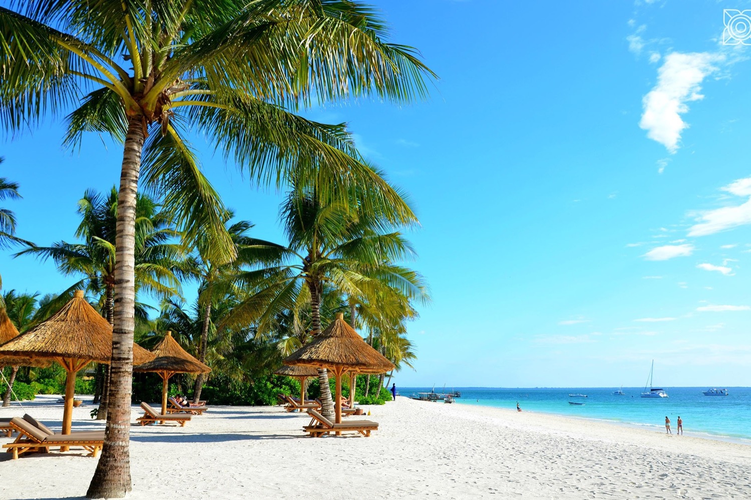 A beautiful white sand beach in Zanzibar with palm trees, thatched umbrellas, and turquoise water.