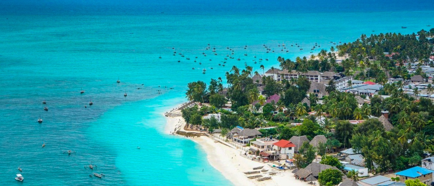 Aerial view of Zanzibar's Nungwi beach with turquoise ocean, many boats, and palm-lined coast.