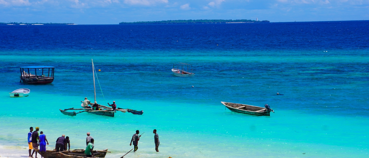 Locals work with traditional boats on the vibrant turquoise waters of a sunny Zanzibar beach.