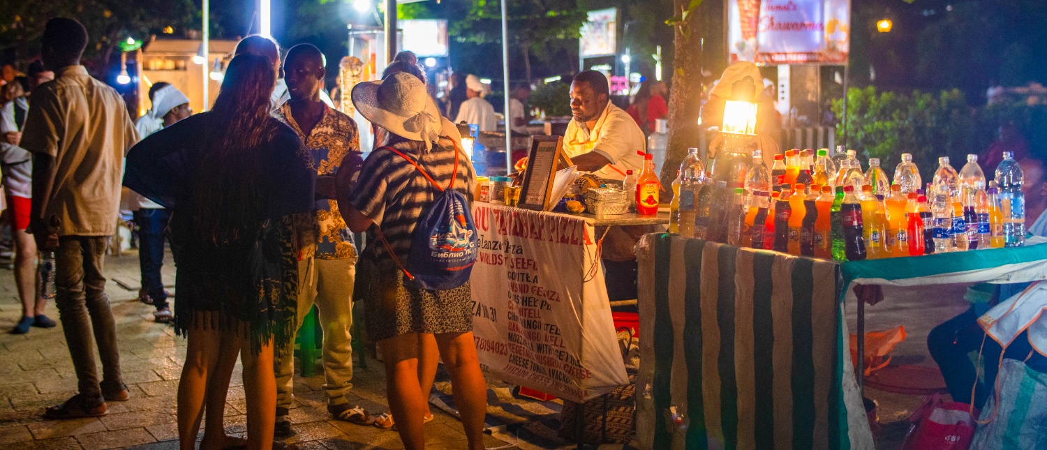 People browse a lively night market stall selling colorful drinks in Zanzibar.