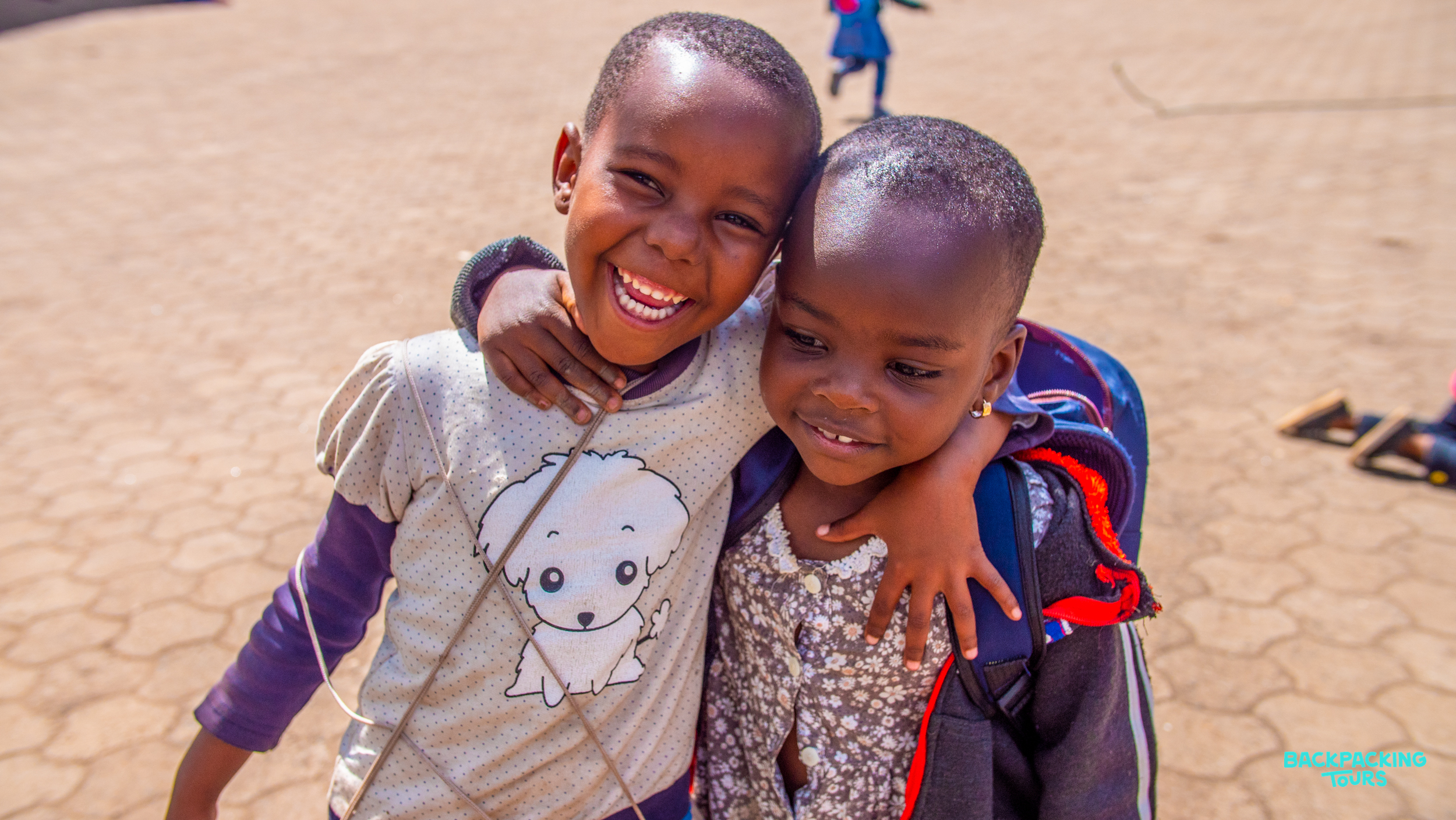 Two young children embrace with wide smiles, sharing a moment of pure joy in Zanzibar.