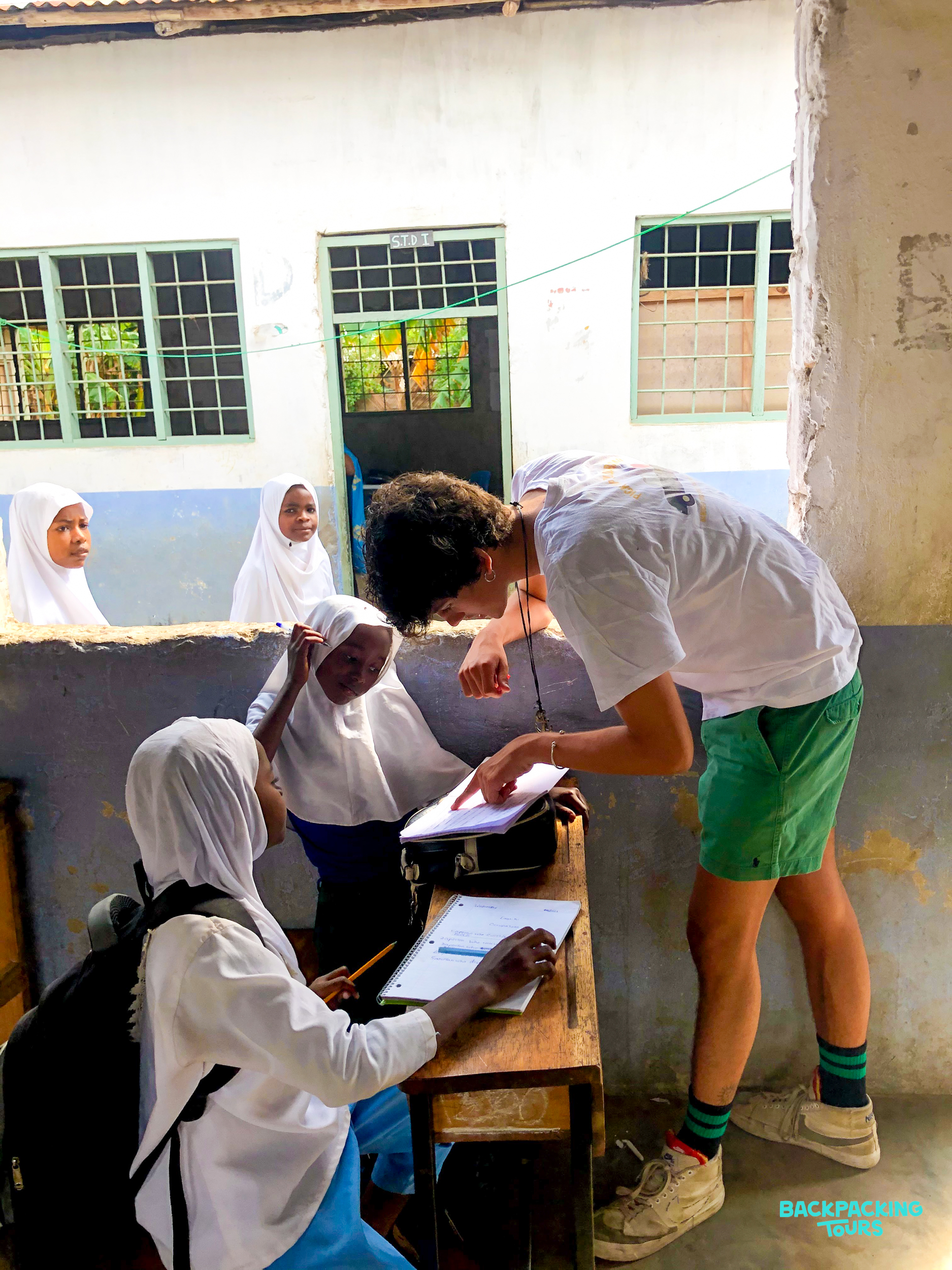 A volunteer points to a book, helping young girls with their lessons at a school in Zanzibar.