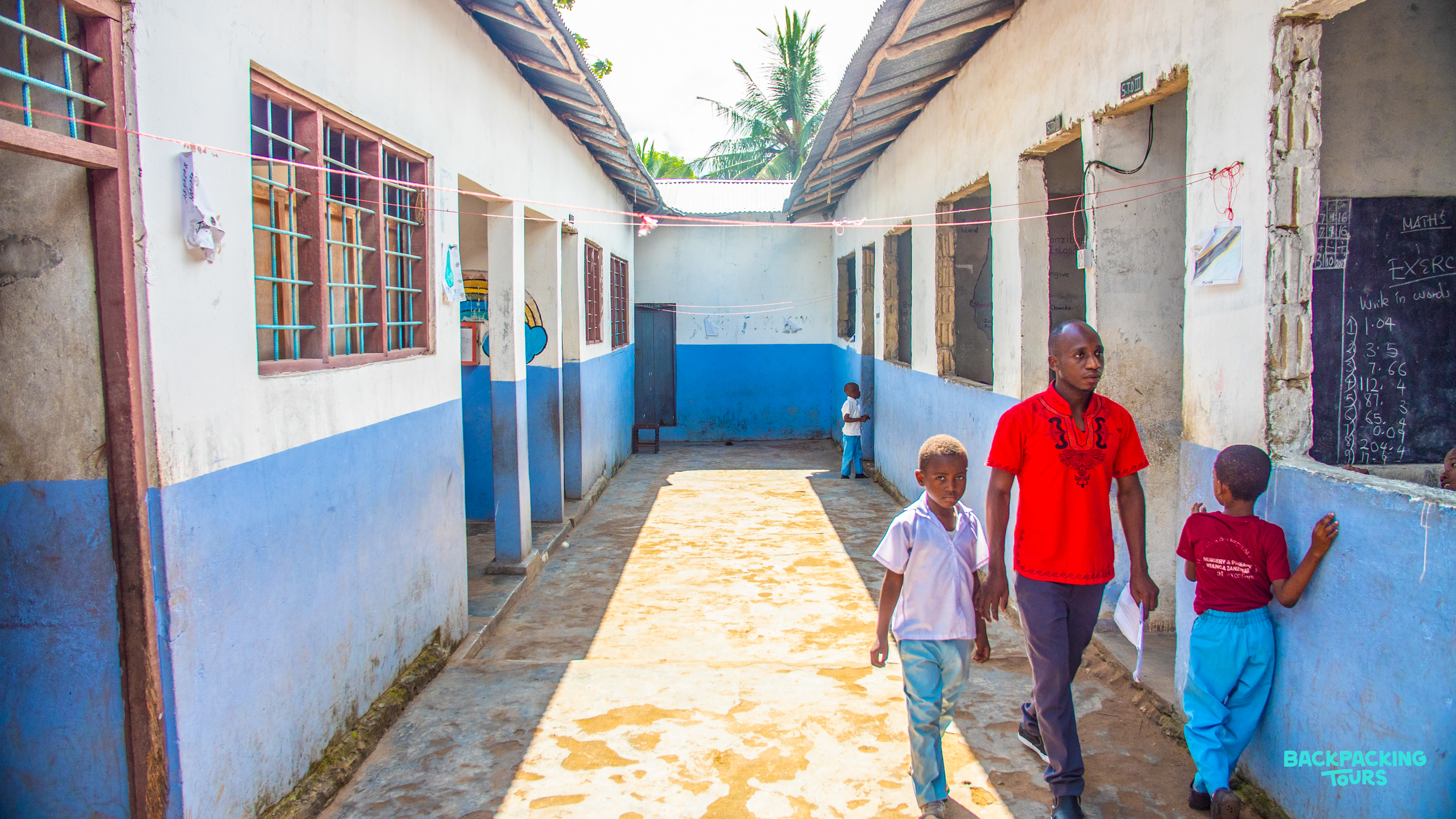 A teacher walks with two young students through a bright school corridor in Zanzibar.