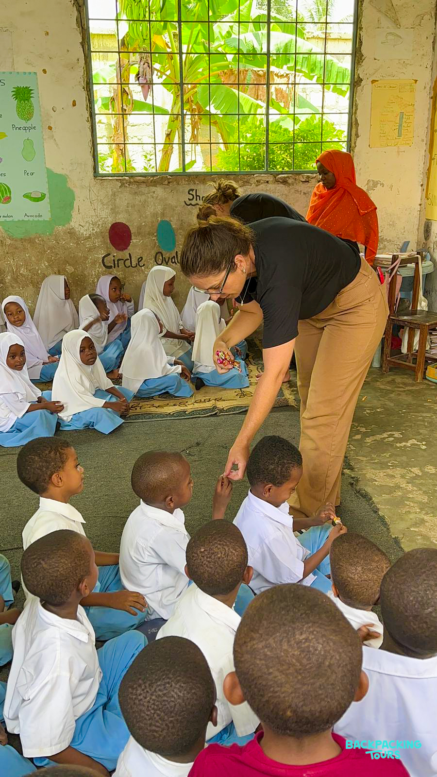 Engaged children in Zanzibar attentively watch a volunteer teacher sharing colorful learning materials.