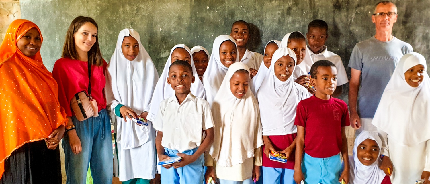 Smiling children and adult volunteers pose together in a classroom in Zanzibar.