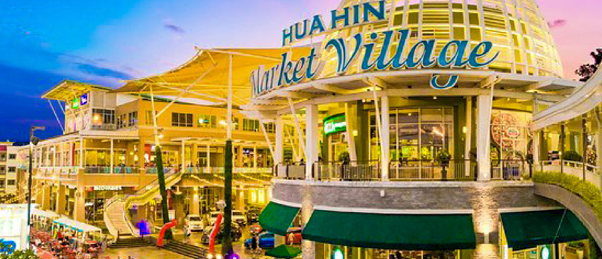 The brightly lit Hua Hin Market Village at dusk, a modern shopping complex with multiple levels.