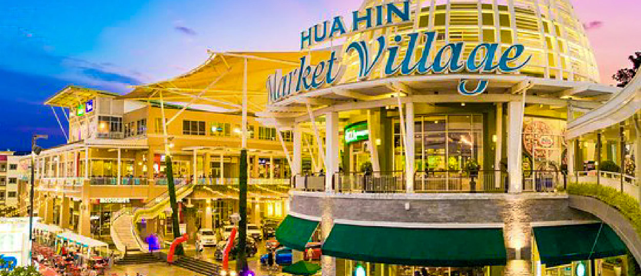 The brightly lit Hua Hin Market Village at dusk, a modern shopping complex with multiple levels.