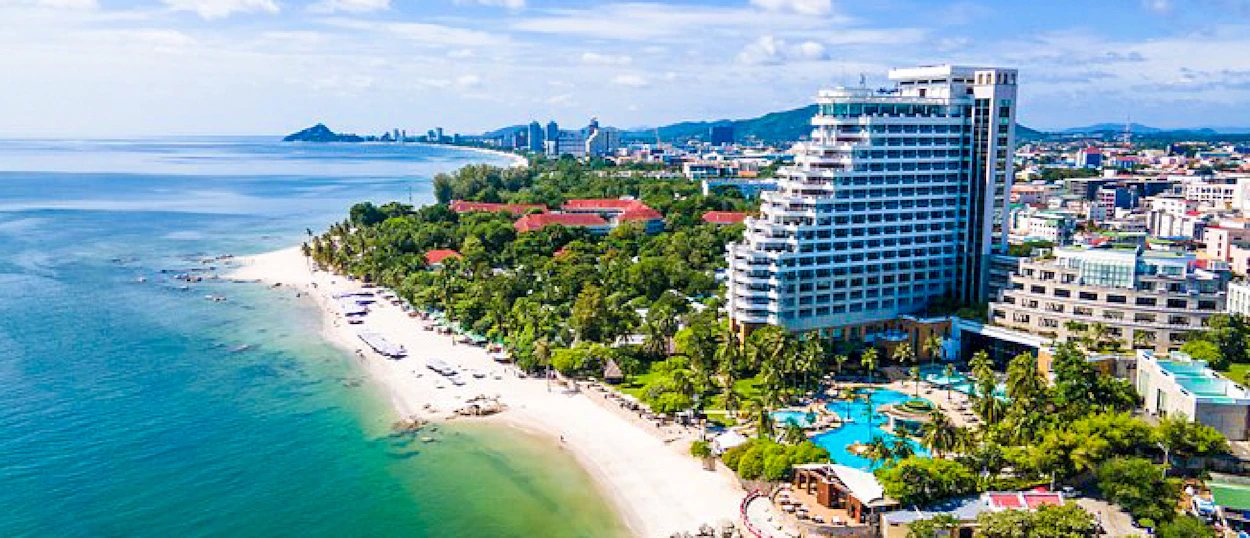 Aerial view of a vibrant coastal city with a long sandy beach, blue ocean, and resort hotels.