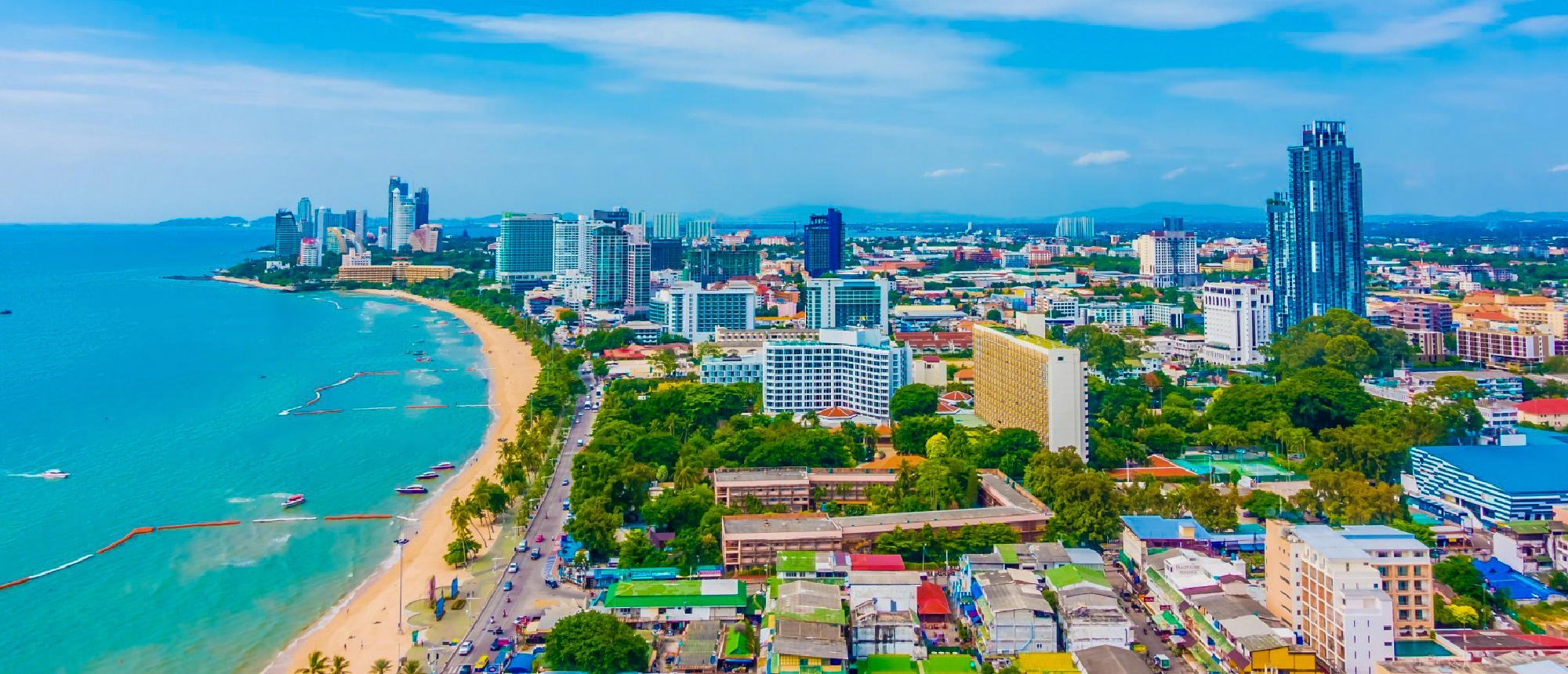 Aerial view of a vibrant coastal city in Thailand featuring a long sandy beach and many buildings.