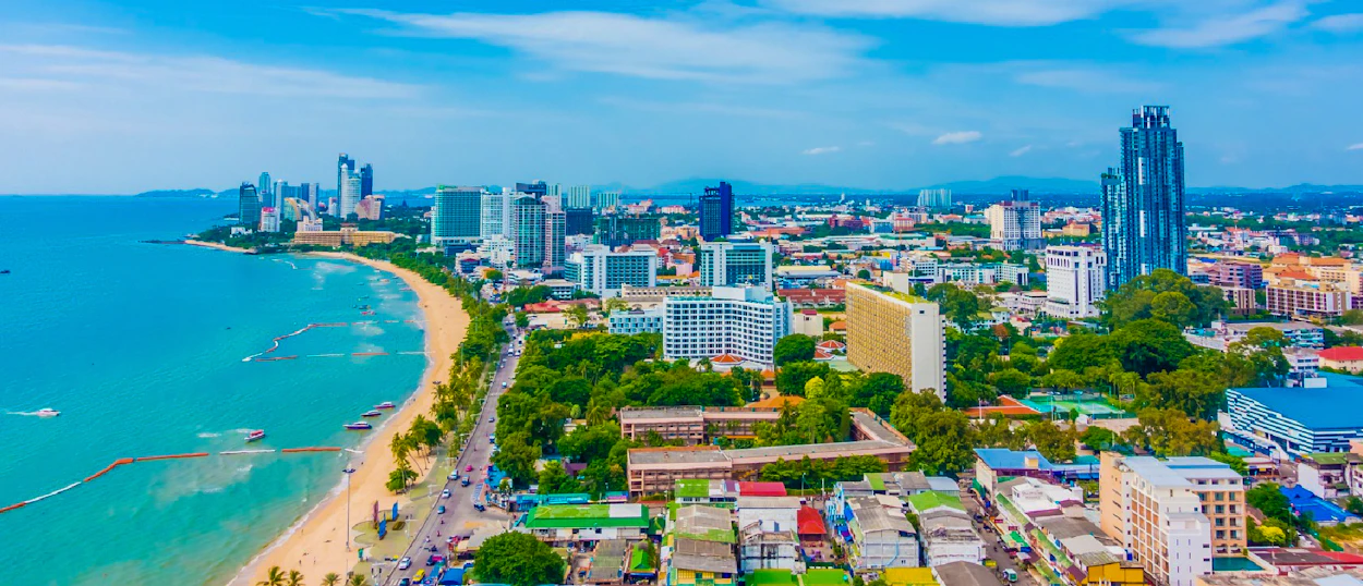 Aerial view of a vibrant coastal city in Thailand featuring a long sandy beach and many buildings.