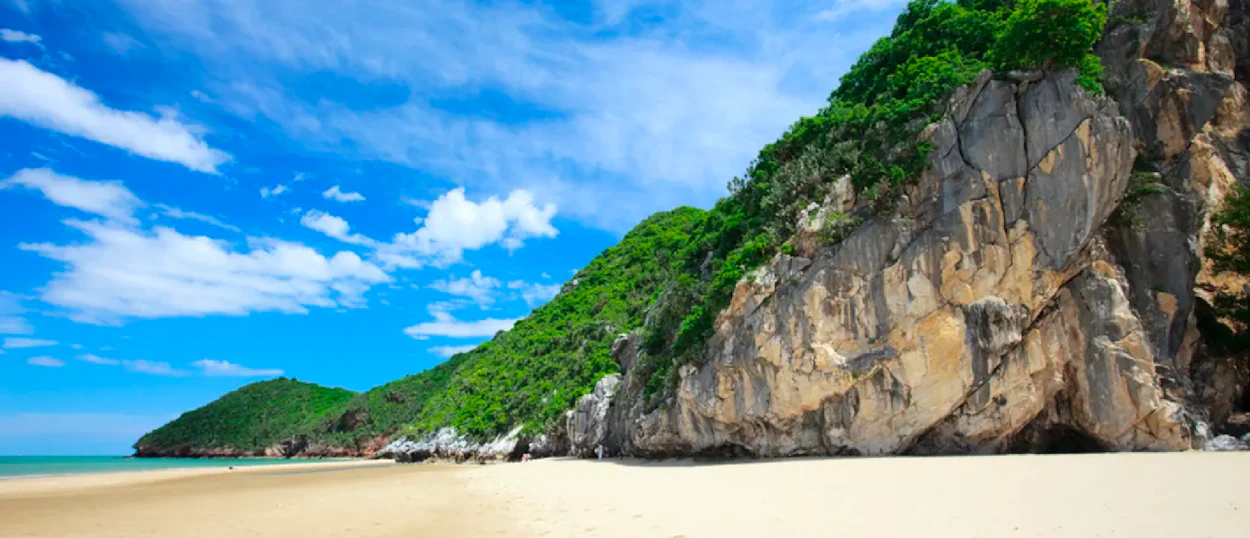 A beautiful sandy beach with lush green cliffs and blue ocean under a bright sky in Pranburi.