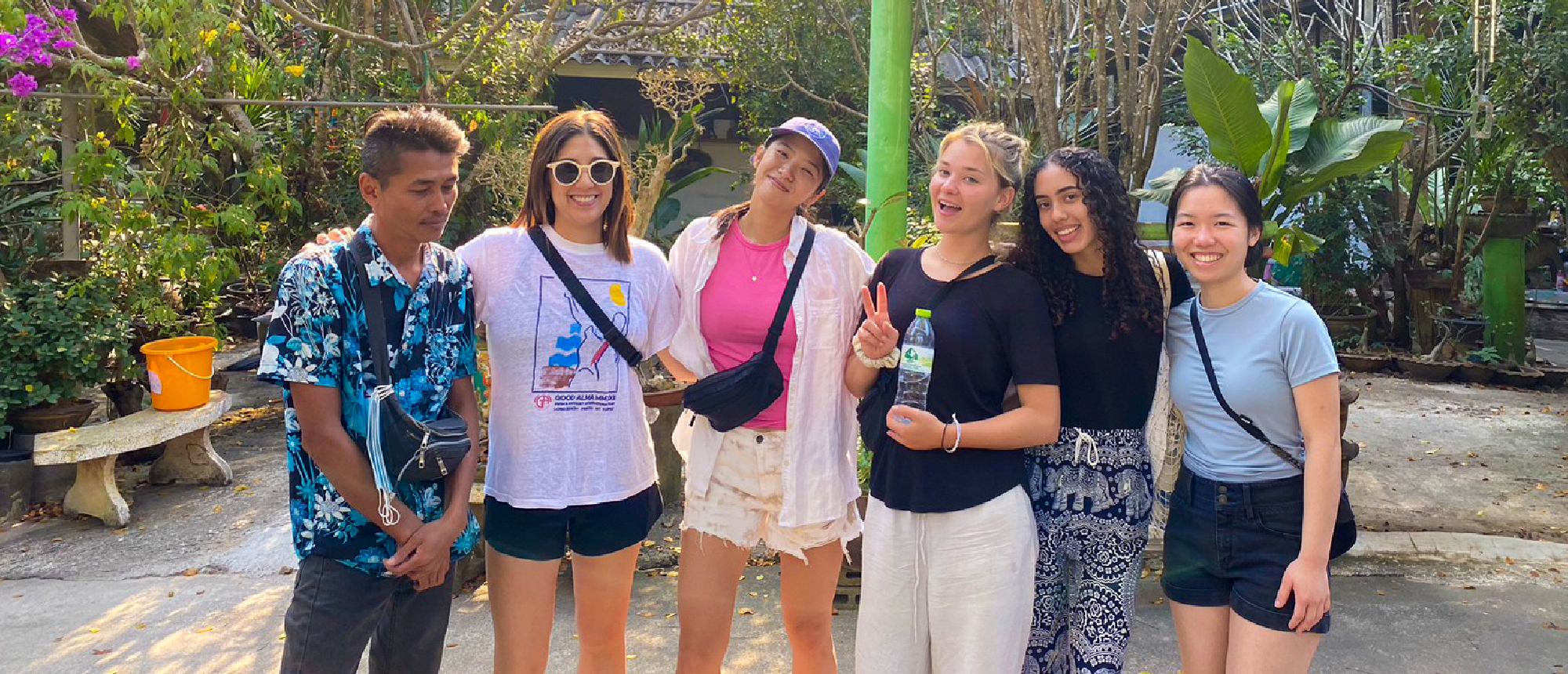 Six happy volunteers and a local guide pose together in a lush outdoor setting in Thailand.