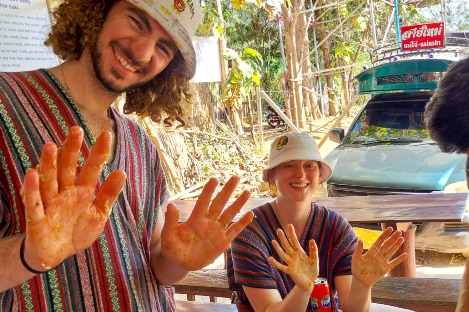 Smiling volunteers in Thailand proudly display hands covered in orange elephant food paste.
