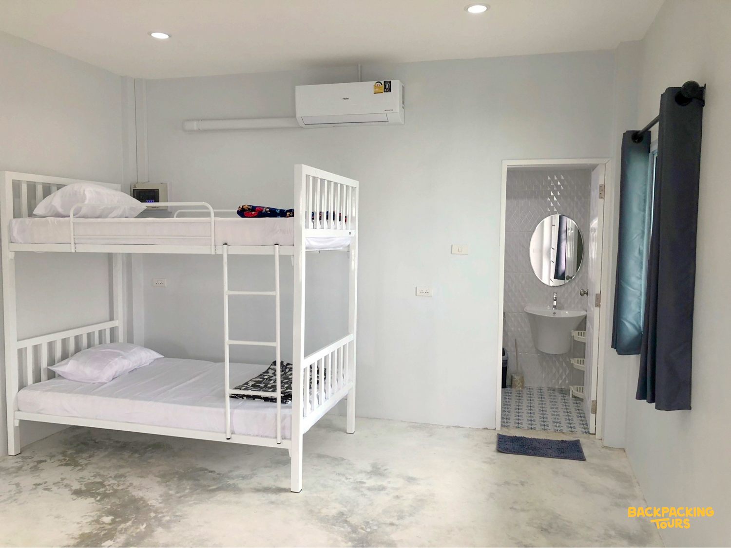 Bright and basic volunteer accommodation in Chiang Mai, featuring white bunk beds and a private bathroom.