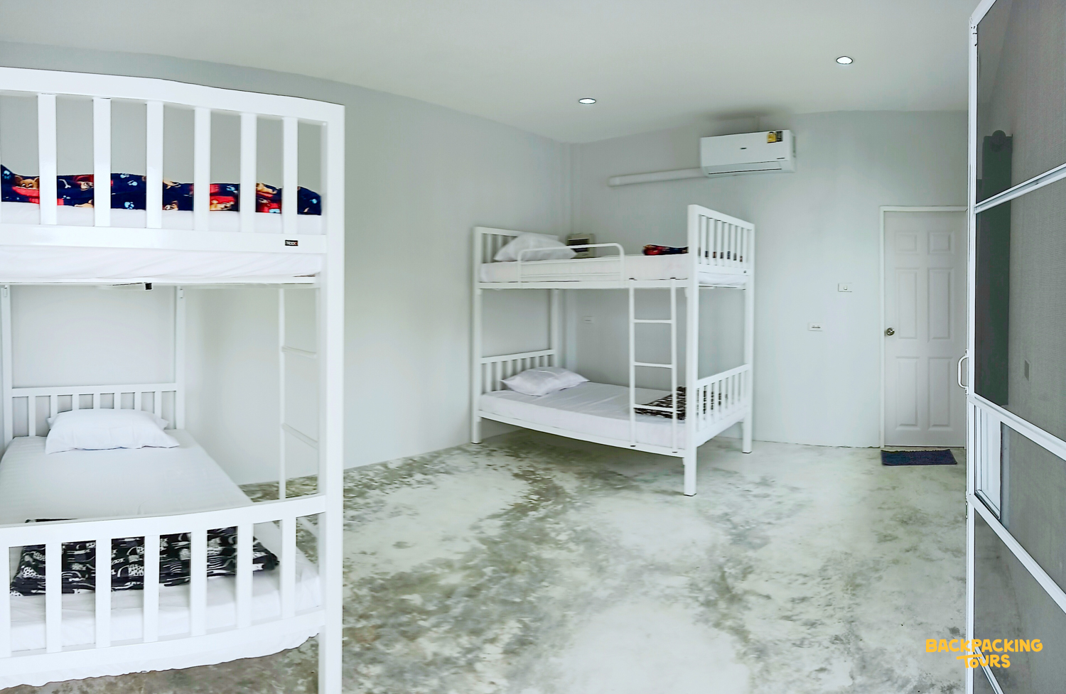 A bright, clean dormitory room with three white bunk beds and concrete floors, ready for volunteers.