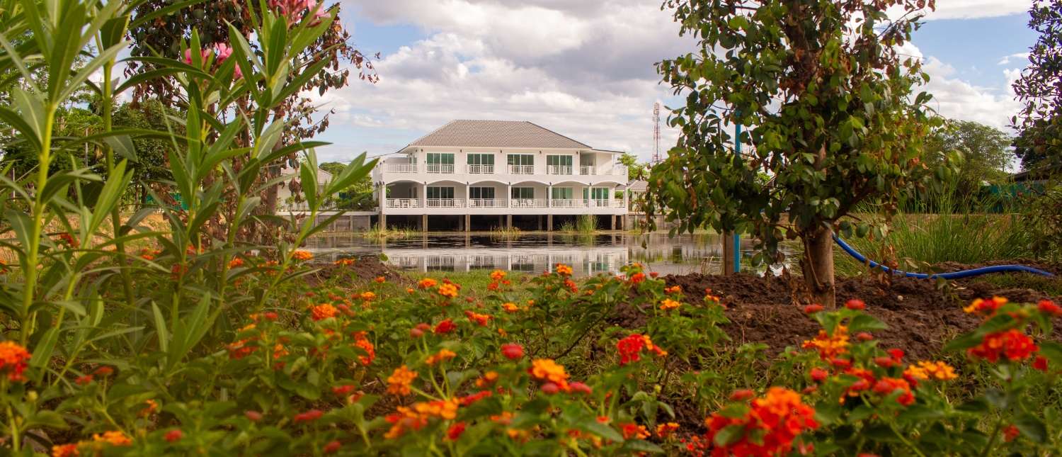 A white multi-story building with balconies stands behind a lush garden of orange and red flowers.