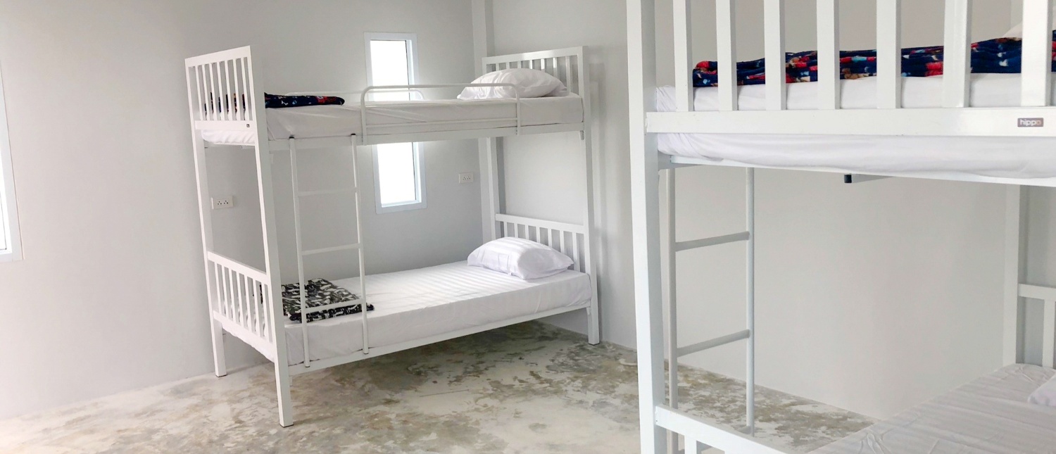 Bright, minimalist dormitory room featuring two white bunk beds with clean white bedding.
