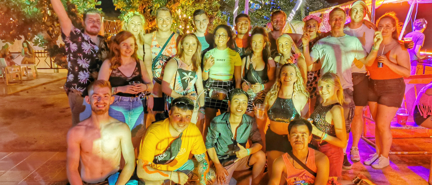 A large group of happy young people posing at a lively outdoor night party on Koh Phangan.
