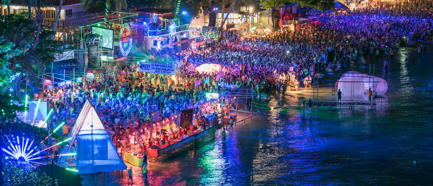A massive crowd dances under vibrant neon lights at the famous Full Moon Party in Thailand.