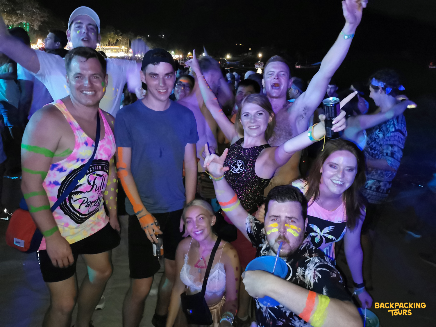 Backpackers with neon paint and glow sticks enjoying the energetic Full Moon Party on Koh Phangan.