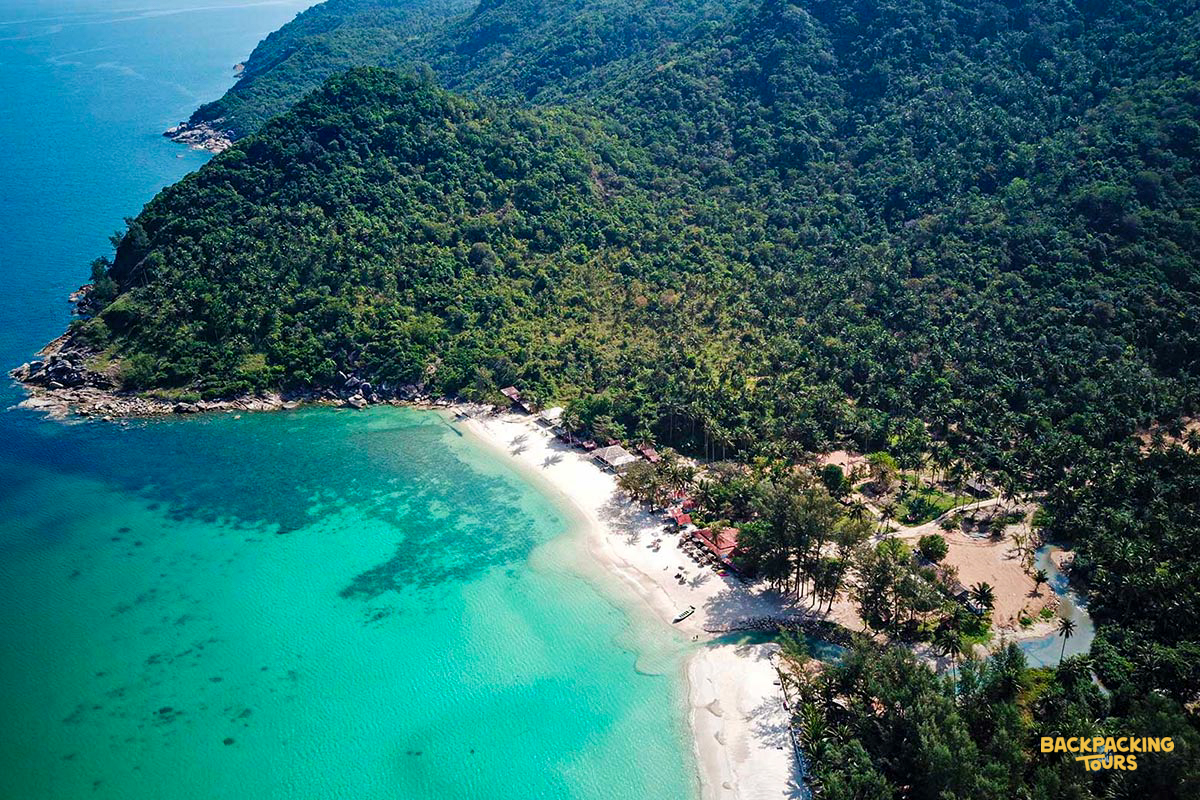 Pristine white sand beach, turquoise ocean, and lush green jungle from above on Koh Phangan.
