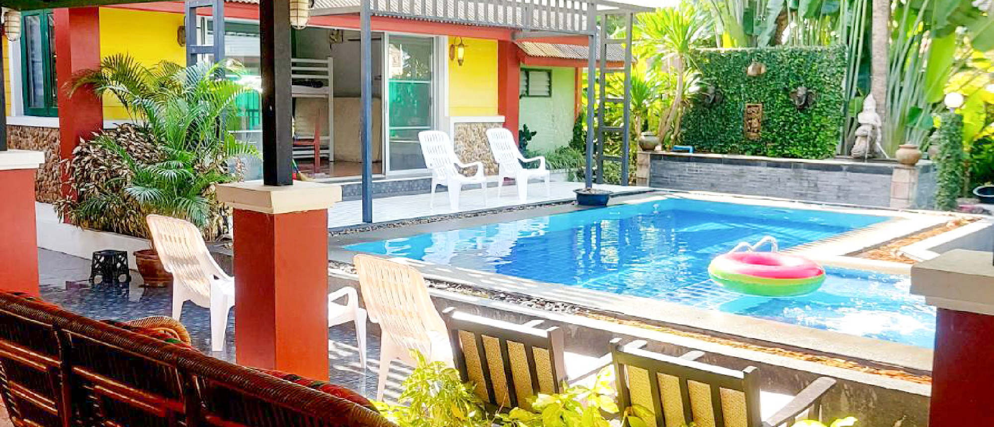 Colorful accommodation building with a swimming pool, lounge chairs, and tropical plants in Thailand.