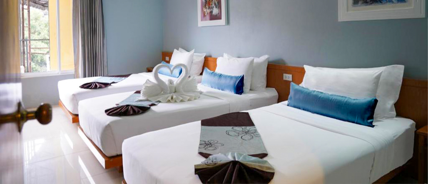 A welcoming hotel room in Bangkok featuring three single beds with white linens and swan towel art.