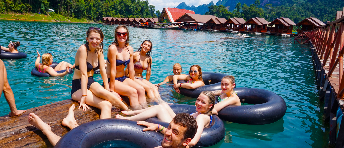 Smiling friends enjoy swimming and tubing in a clear lake with floating bungalows in Khao Sok.