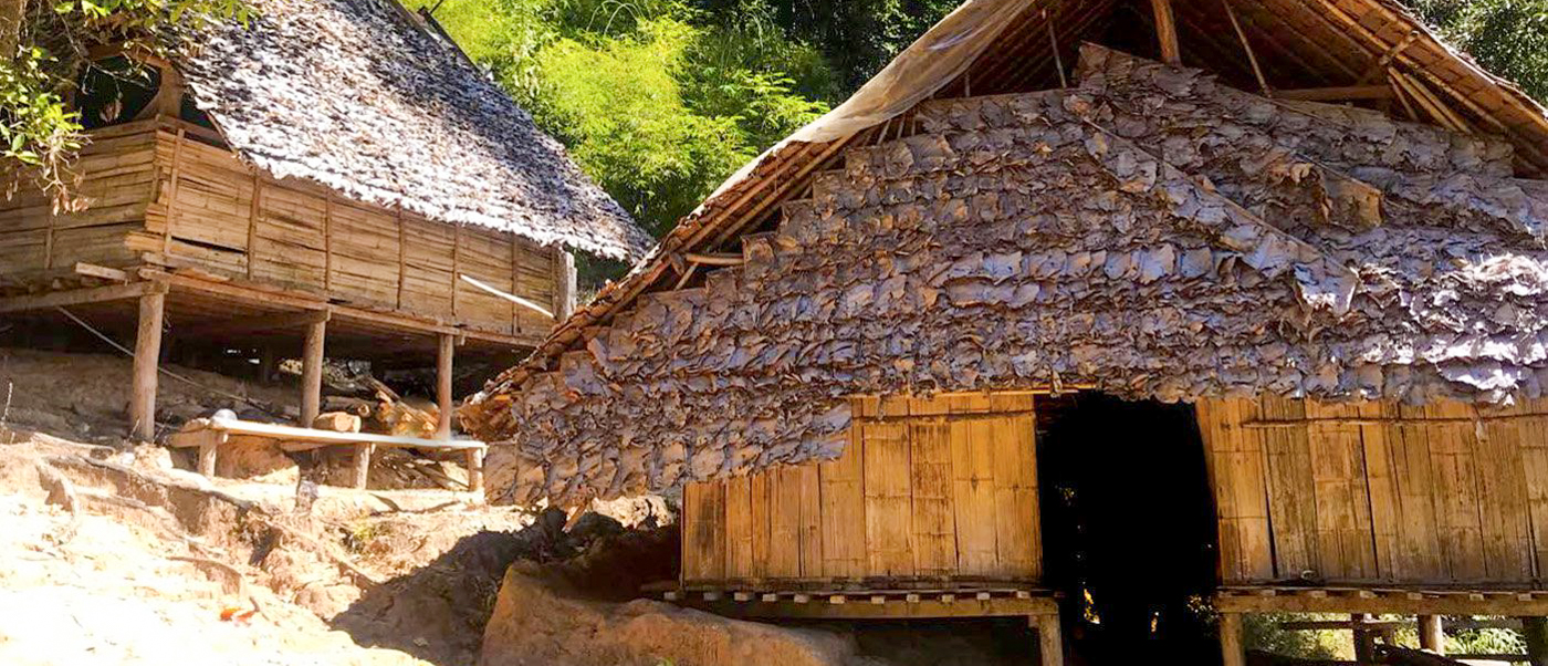 Two rustic bamboo huts with elevated floors and thatched roofs in a hill tribe village in Chiang Mai.