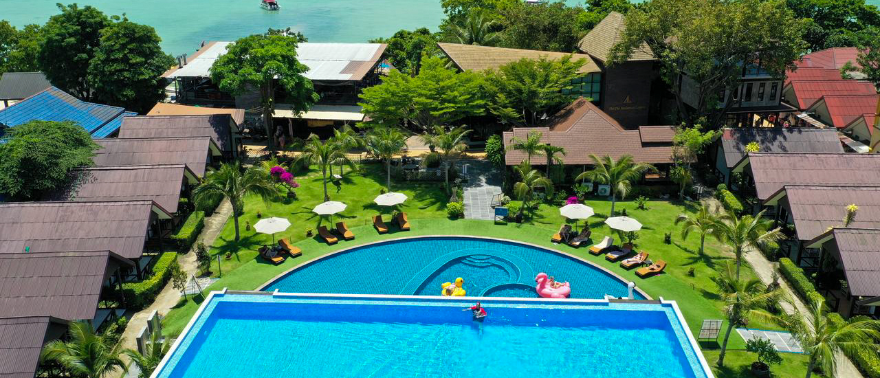 Aerial view of a vibrant resort with swimming pools, bungalows, and turquoise sea in Koh Phi Phi.