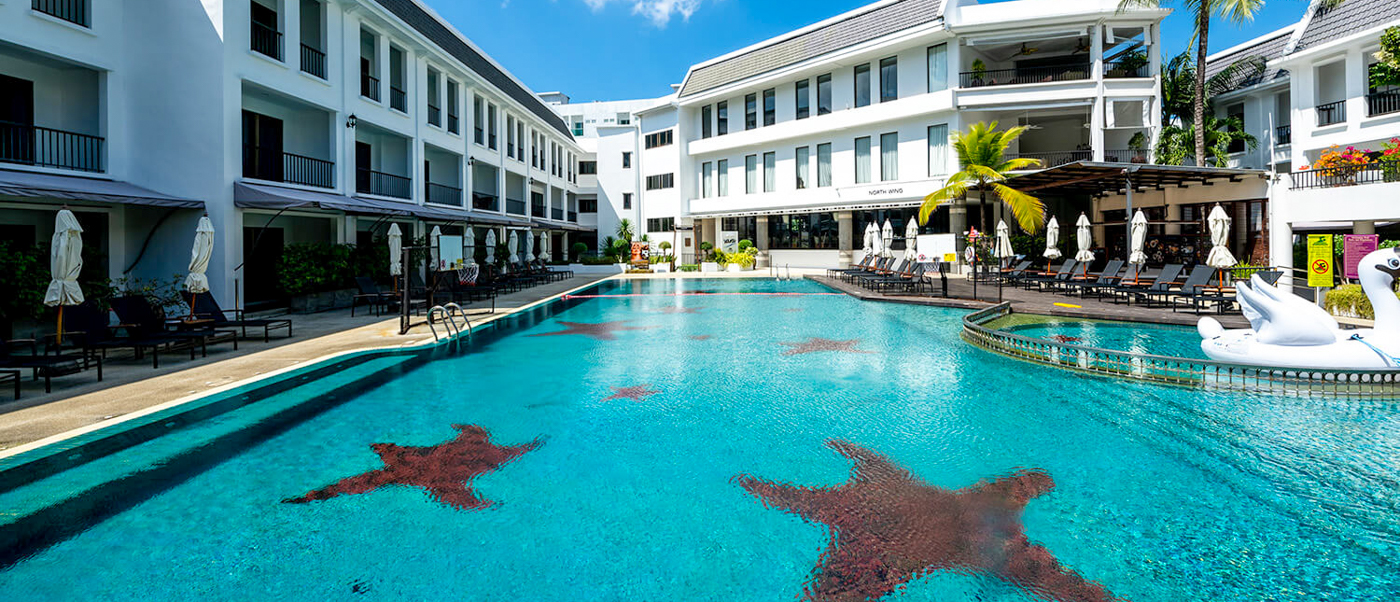 A large, inviting resort swimming pool with starfish patterns, sun loungers, and white buildings in Phuket.