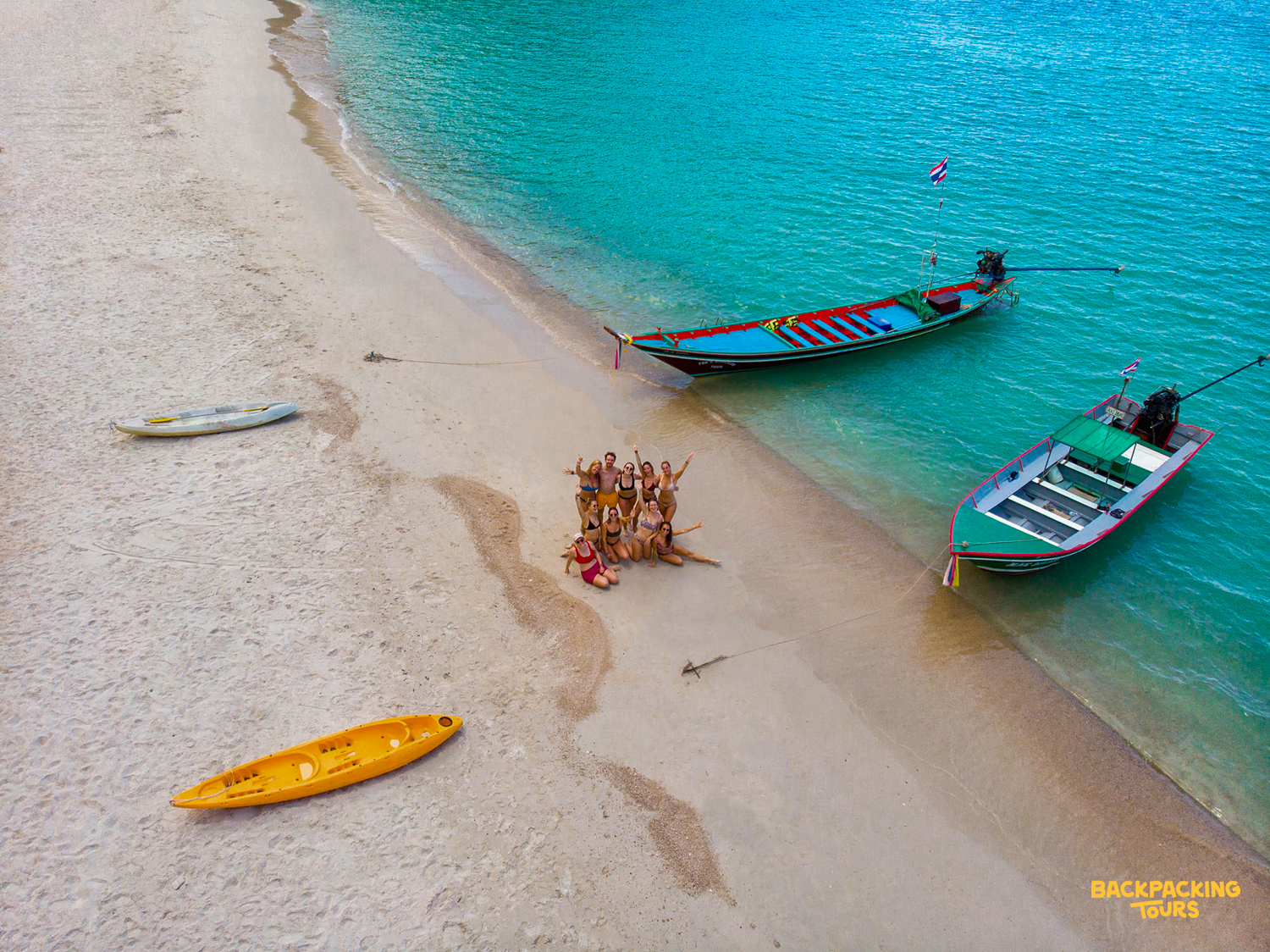 Aerial view of longtail boats anchored off a white sand beach in Koh Phangan, Thailand