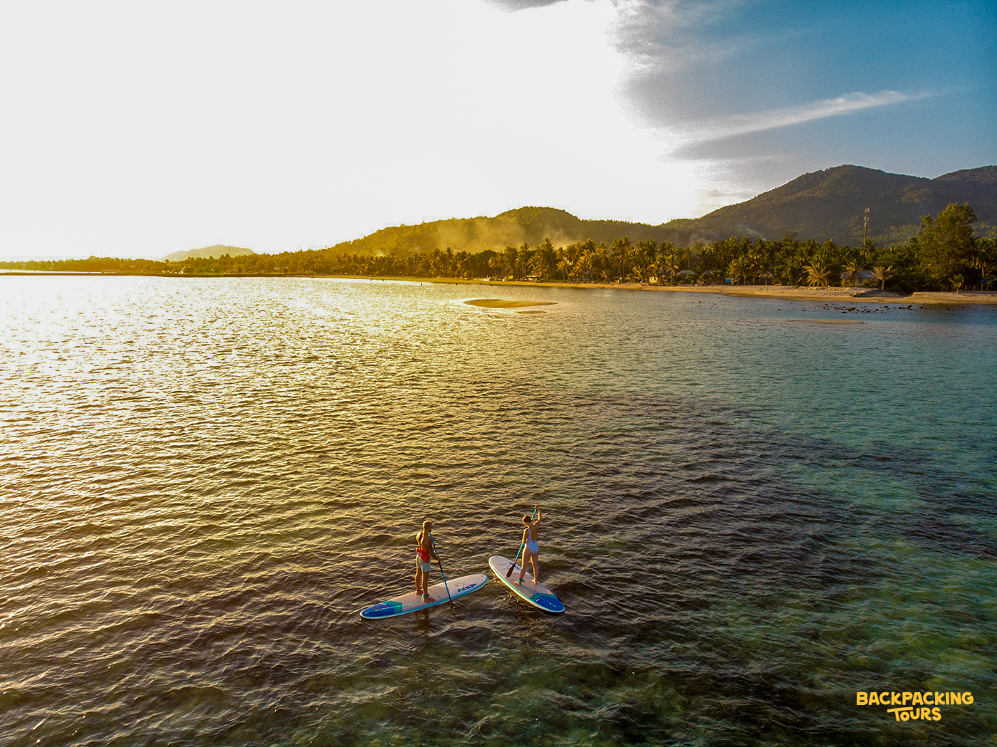 Two people paddleboarding on the clear, calm waters of Koh Phangan during a golden sunset.