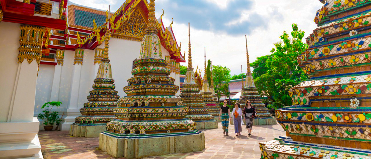Three people walk among ornate golden stupas at a beautiful temple in Bangkok.