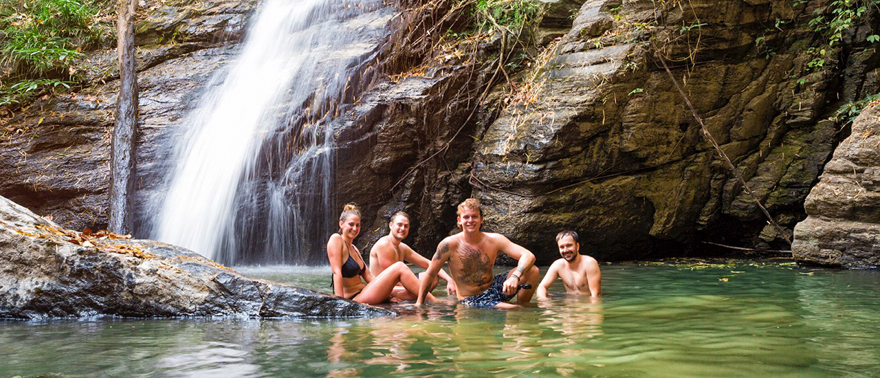 Four happy travelers cool off in a natural pool at the base of a waterfall in Chiang Mai.