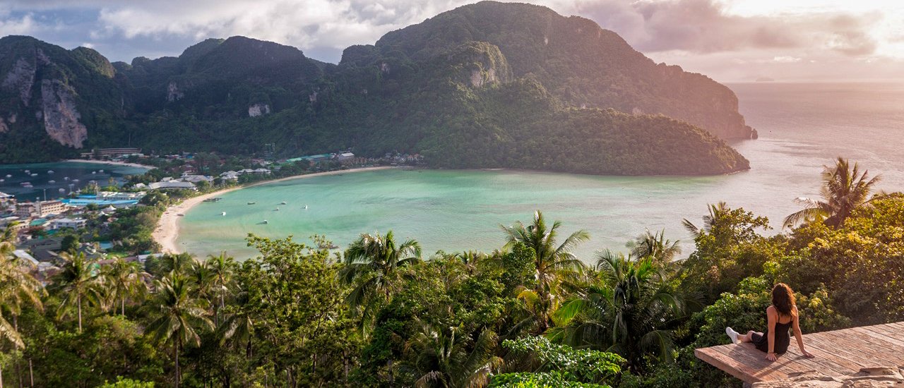 A woman enjoys the beautiful sunrise view over Koh Phi Phi's tropical bay from a viewpoint.