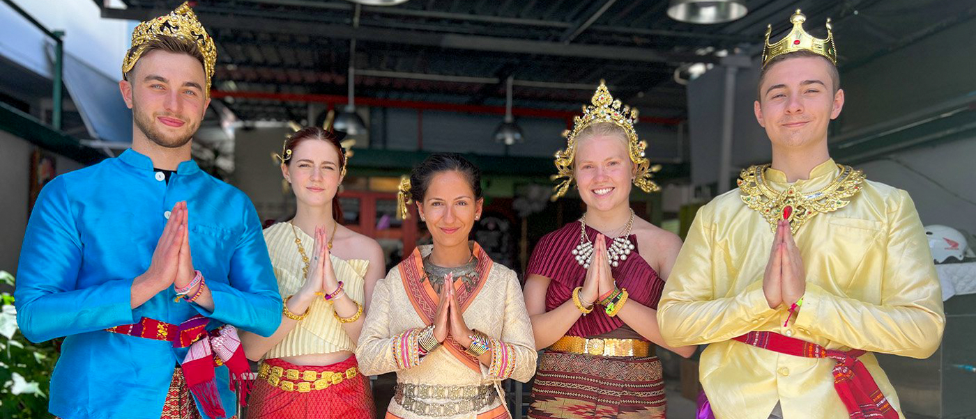 Five people in vibrant traditional Thai clothing performing the respectful wai gesture in Bangkok.