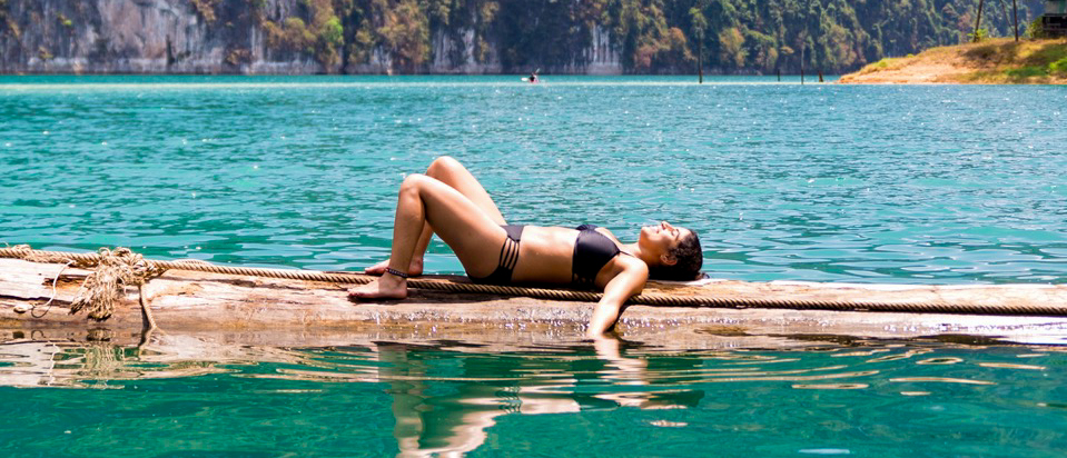 A woman in a bikini floats peacefully on a log in the clear turquoise waters of Khao Sok.