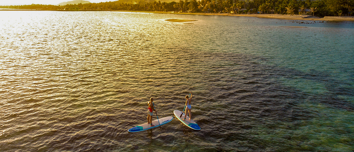 Adventurers paddleboarding on the serene, golden waters of Koh Phangan during a stunning sunset.