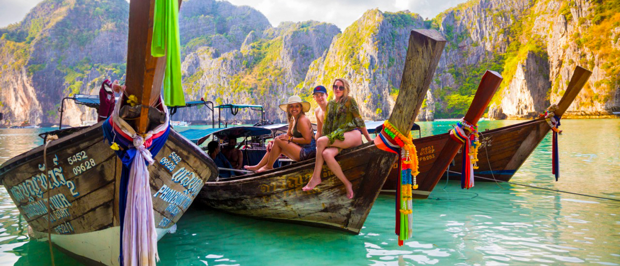 Three friends sit on a longtail boat in the turquoise waters of Koh Phi Phi, Thailand.