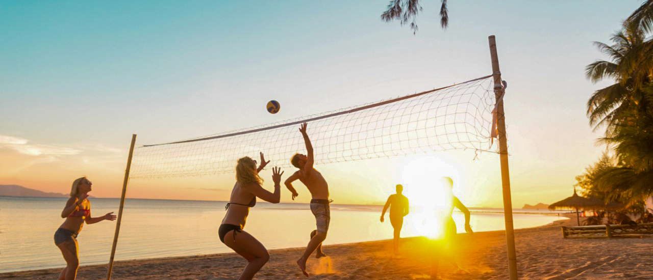 People playing beach volleyball on a sandy beach at sunset in Koh Phangan, Thailand.
