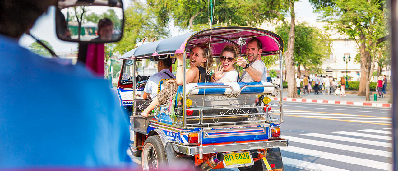 Happy tourists enjoy a lively tuk-tuk ride through the bustling streets of Bangkok, Thailand.