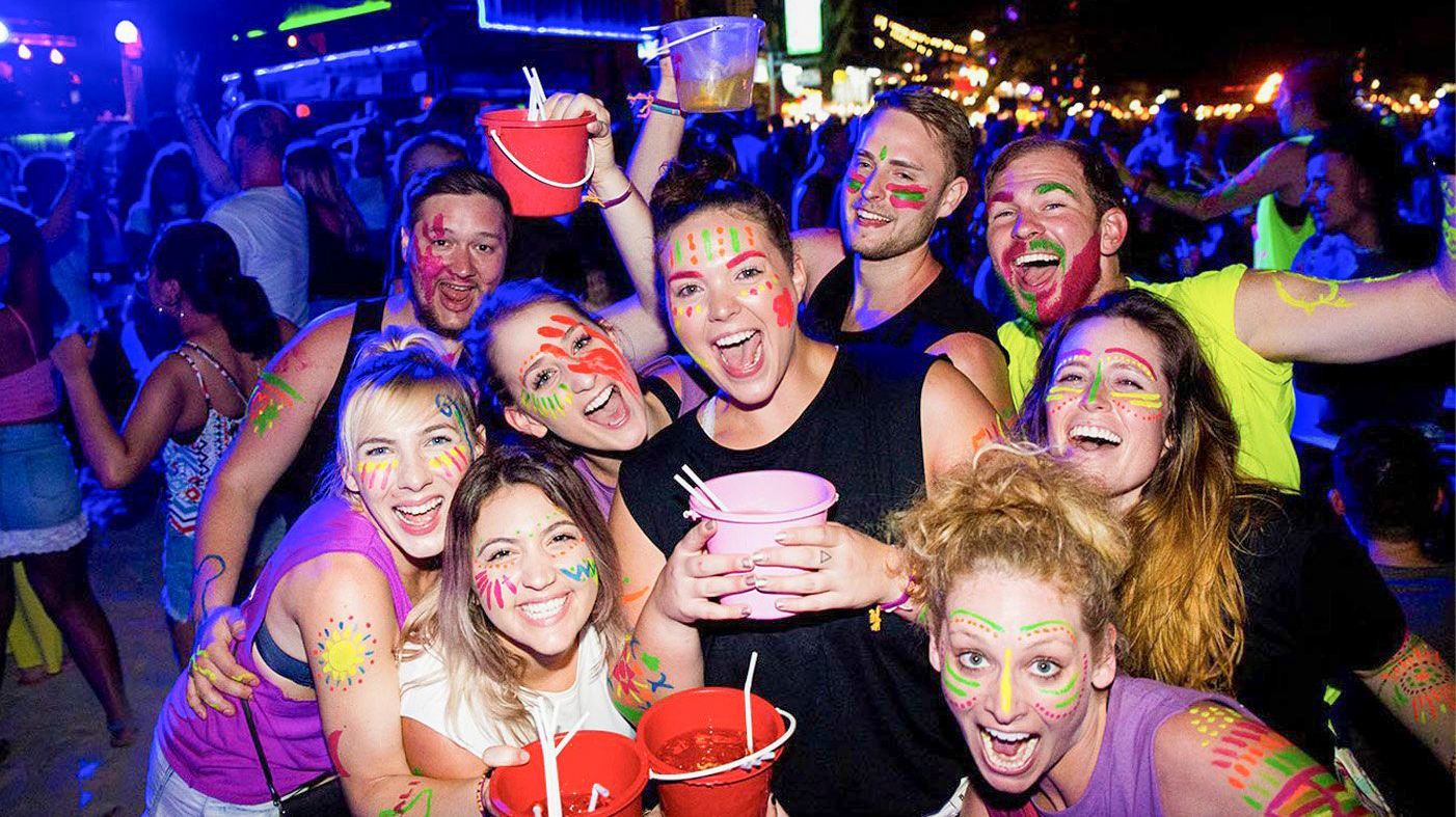 A group of happy backpackers with neon paint enjoying a lively night party in Koh Phangan.