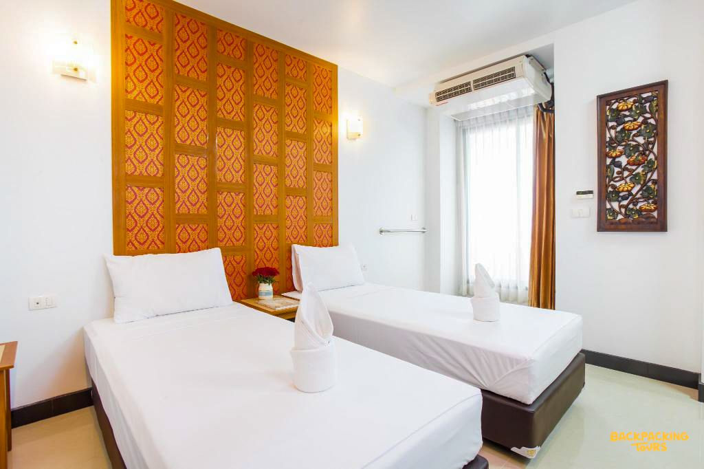 A clean hotel room in Bangkok with two single beds and traditional Thai decor.