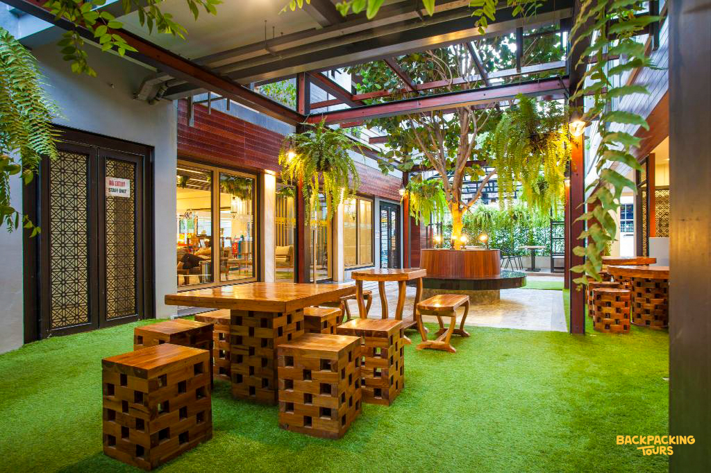 A tranquil outdoor courtyard with wooden tables and lush green plants, perfect for relaxing at your Bangkok accommodation.