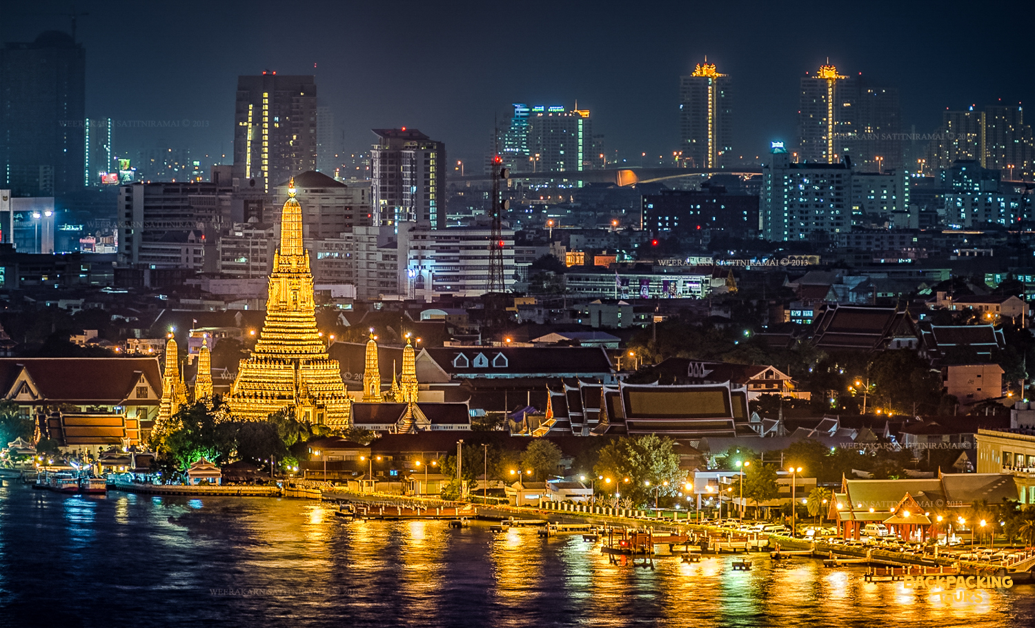 Wat Arun temple glows golden beside the Chao Phraya River at night in Bangkok.