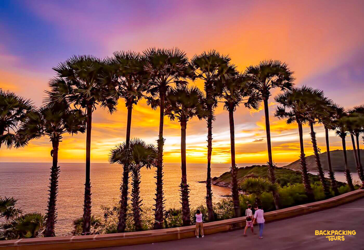 Palm trees silhouette against a magnificent sunset over the ocean, with people enjoying the view in Phuket.